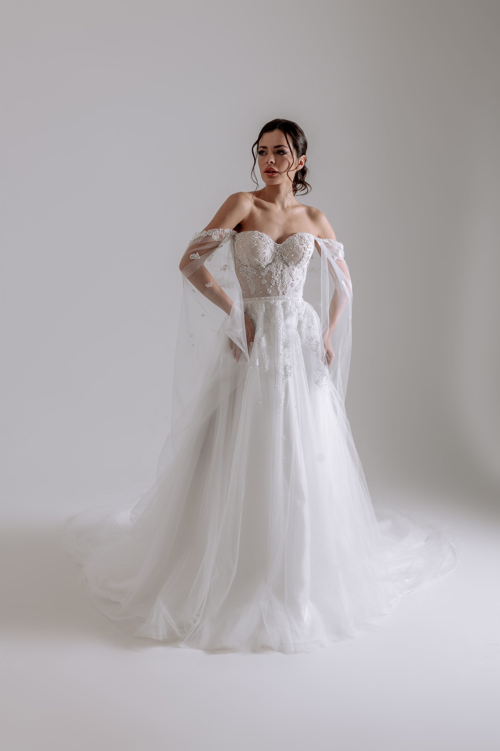 A-Linie Brautkleid aus Tüll und Glitzerspitze, herförmige Corsage nude unterlegt, versteckte Schnürung an der inneren Corsage, Glitzergürtel, Off-Shoulder Cape abnehmbar, sanfter Spitzenverlauf in den Rock, Schleppe 50cm